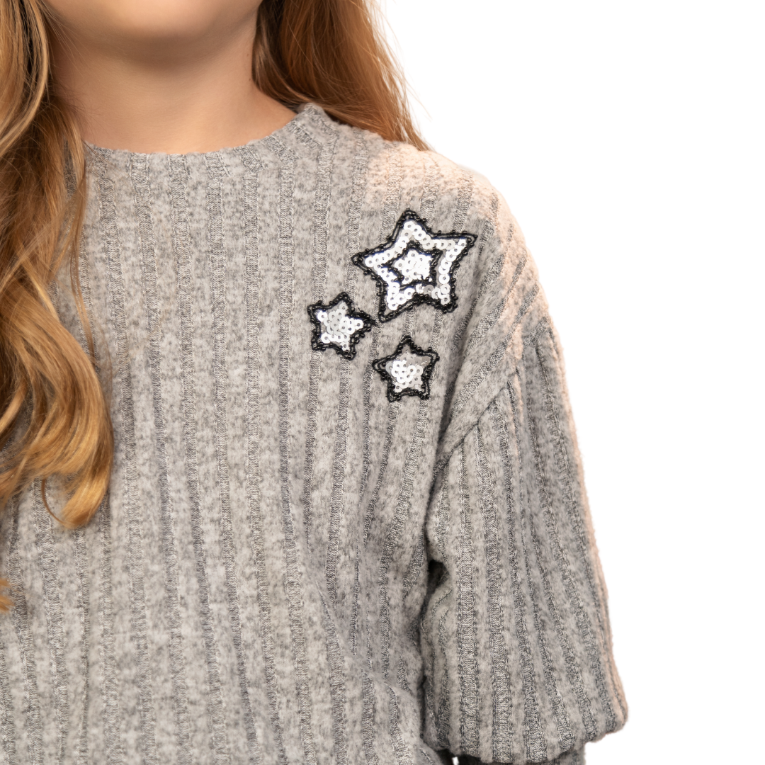 Nahaufnahme der glänzenden Pailletten-Sterne auf dem grauen Pullover