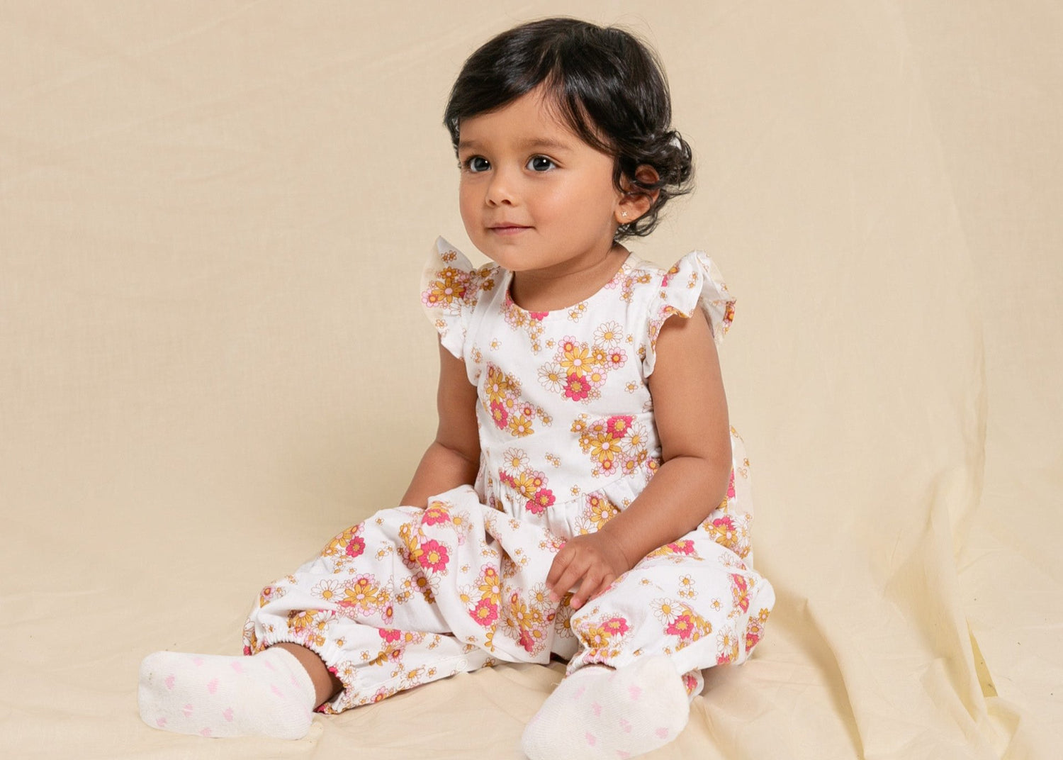 Lächelndes Baby-Mädchen in einem geblümten Jumpsuit.