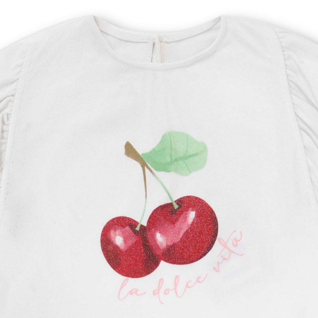 Nahaufnahme vom glitzernden Kirschen-Print auf weißem T-Shirt und doppeltem Rüschenvolant der karierte Shorts.