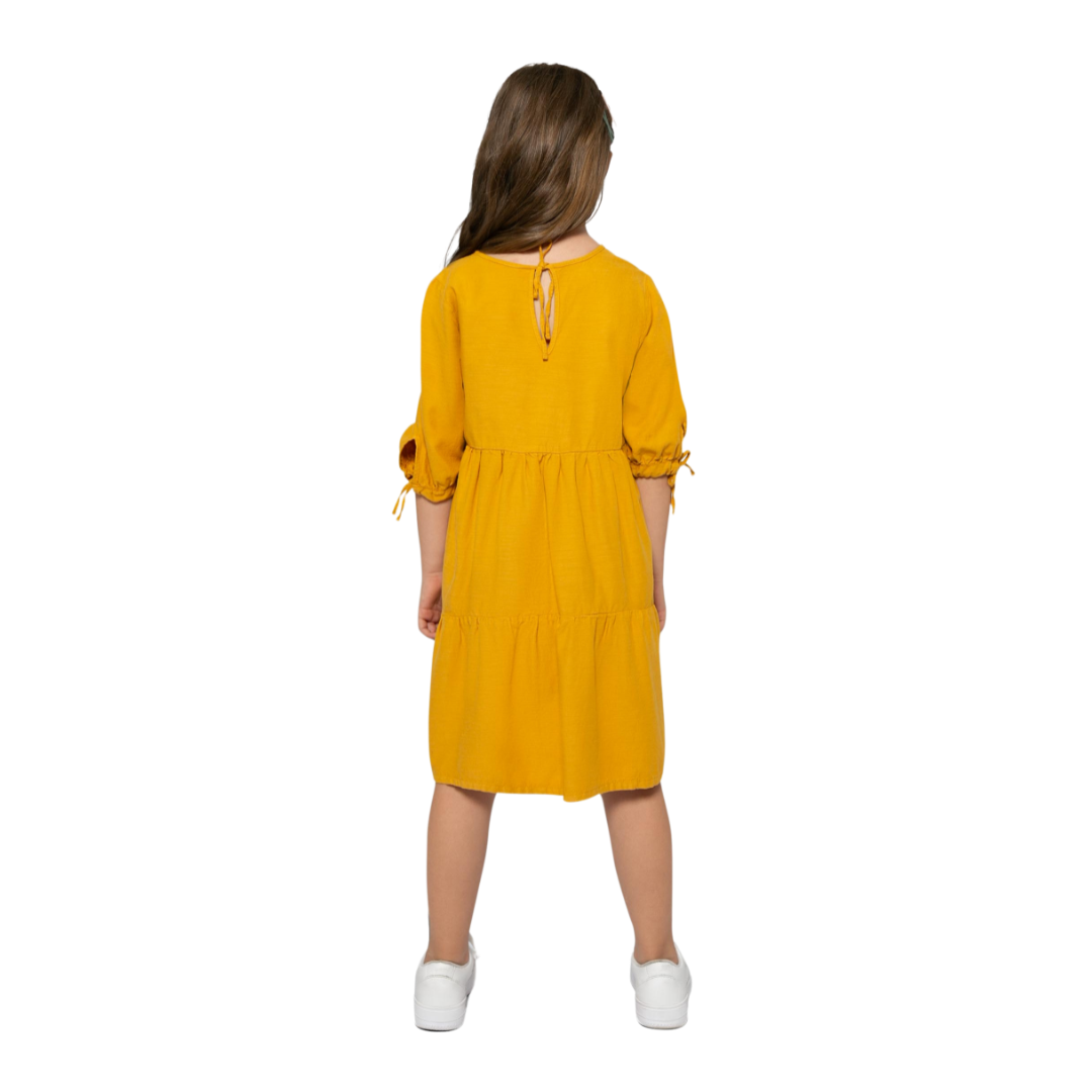 Mädchen trägt das senffarbene Kleid von hinten mit schöner Schleifen
