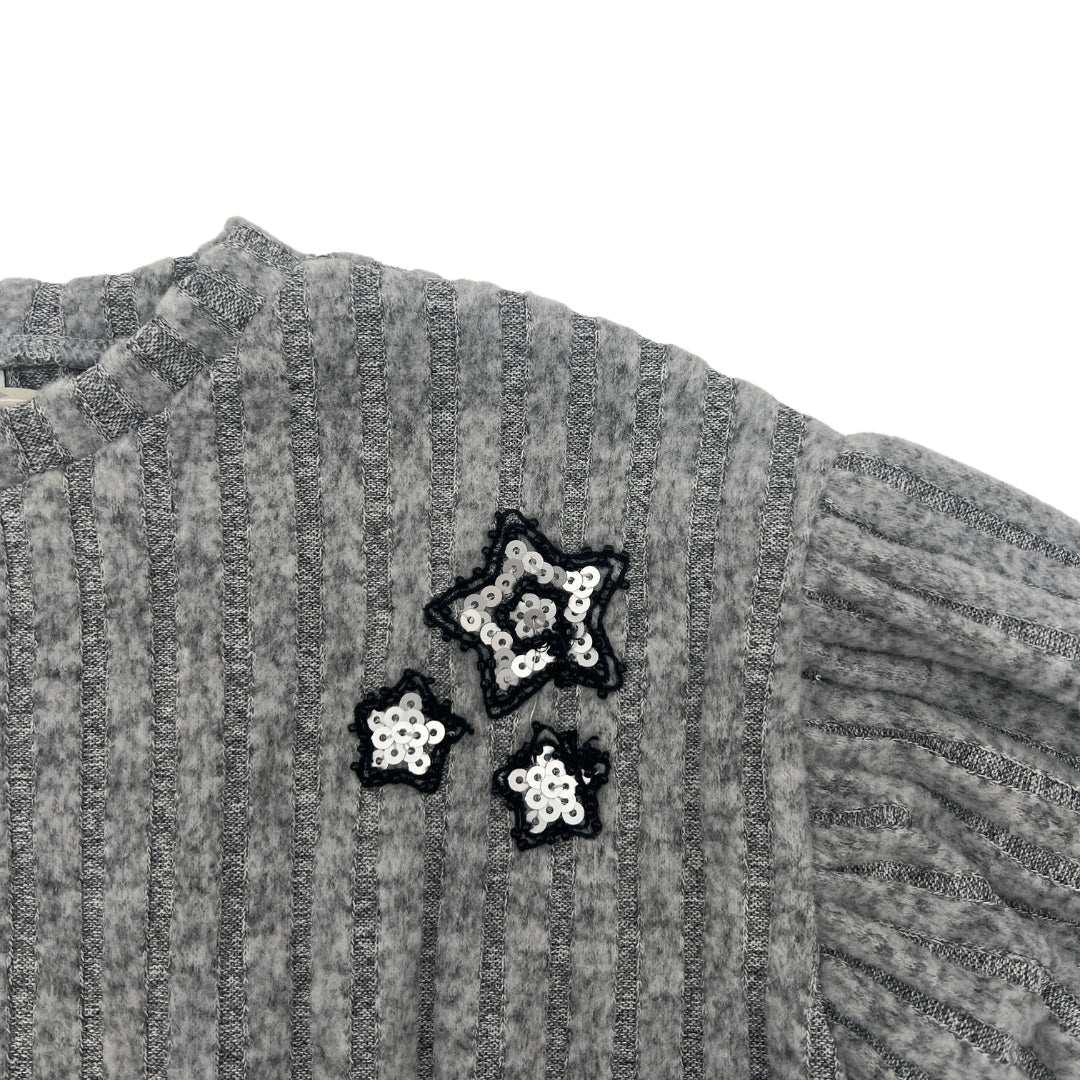 Nahaufnahme der Pailletten-Stickerei auf dem grauen Pullover.