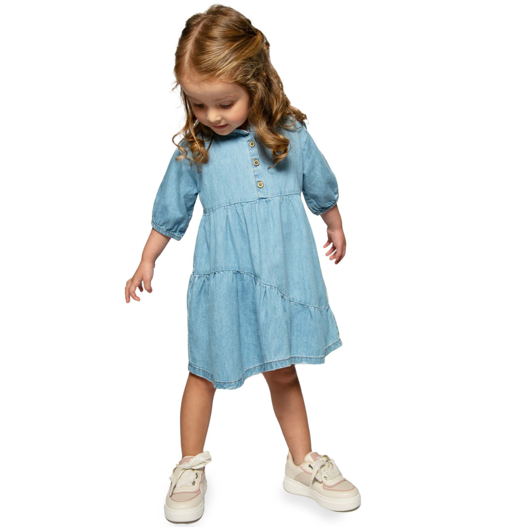 Mädchen trägt das stilvolle Jeanskleid mit 3/4-Ärmeln und asymmetrischem Schnitt, ideal für einen modernen und bequemen Look.