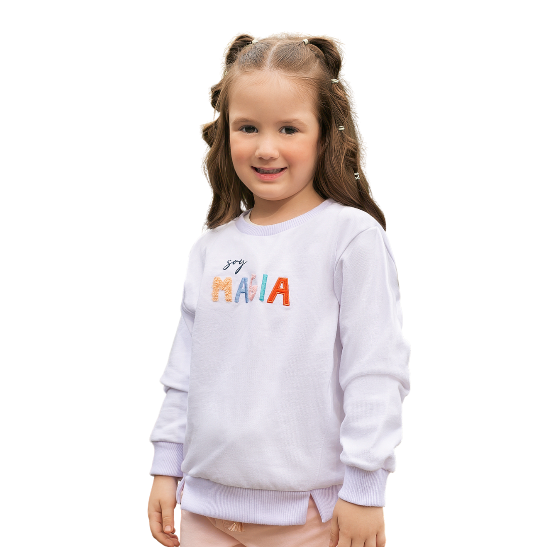 Glückliches Mädchen trägt den weißen Pullover mit 'Soy magia' Stickerei.