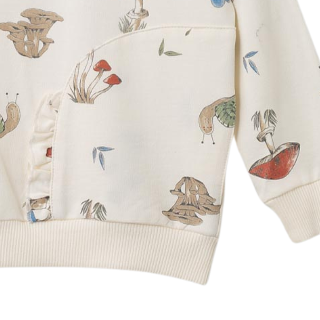 Nahaufnahme des fröhlichen Pilzmusters und des süßen Rüschendetails des beigen Pullovers, ideal für kleine Entdeckerinnen.