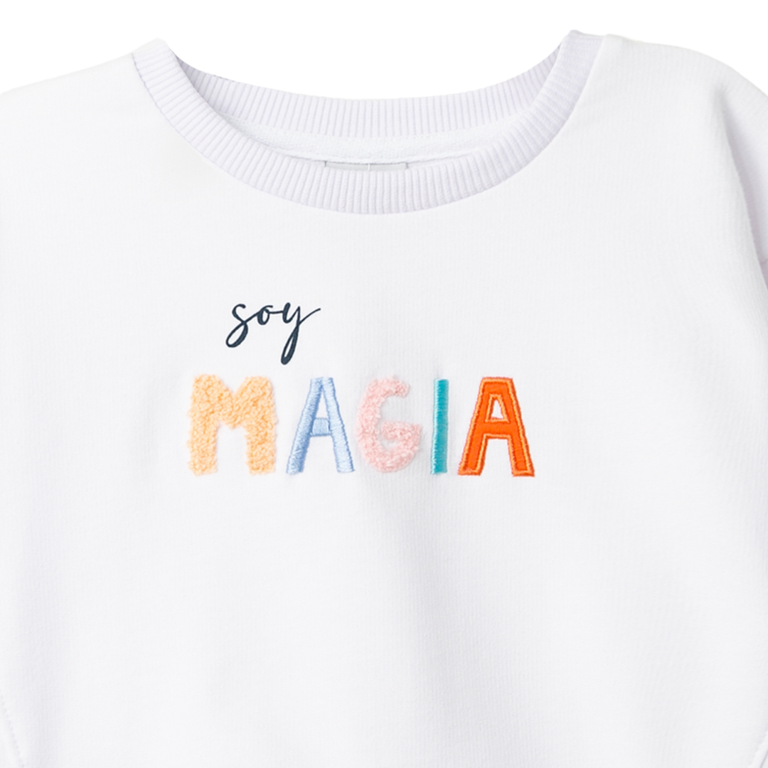 Detailansicht des „Soy magia“-Schriftzugs mit spürbaren Buchstaben und doppeltem Saumschnitt.