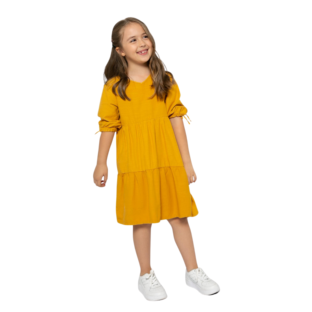 Mädchen trägt das elegante senffarbene Kleid mit Bändern