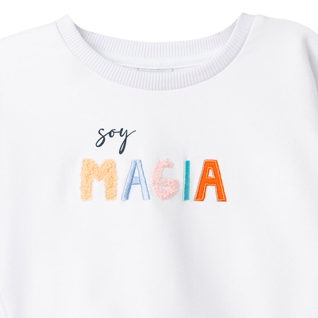 Nahaufnahme der 'Soy magia' Stickerei auf dem weißen Mädchen-Pullover.