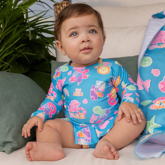 Fröhliches Baby sitzt lachend im blauen Badeanzug mit Volant, bereit für den Sommer.