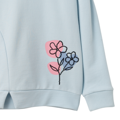 Nahaufnahme der zarten Paillettenblume und des feinen Bundschnitts des hellblauen Mädchenpullovers.
